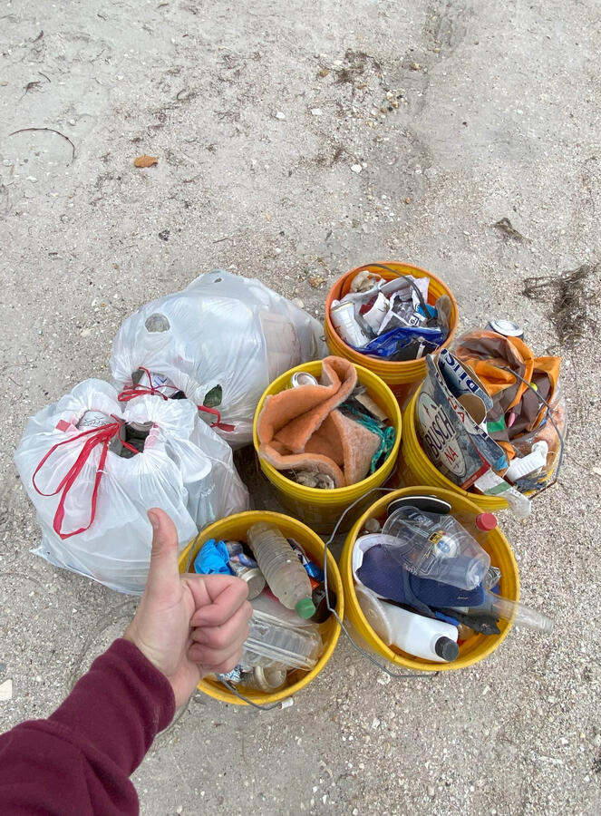 Palma Sola Causeway A volunteer gives a thumbs-up beside several yellow buckets and trash bags filled with collected litter after a cleanup.